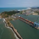 Vista aérea de um porto brasileiro, com docas, guindastes e navios junto à costa.