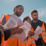 Voluntários usando coletes laranja distribuem cartazes de pessoas desaparecidas ao ar livre