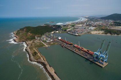 Vista aérea de um porto brasileiro, com docas, guindastes e navios junto à costa.