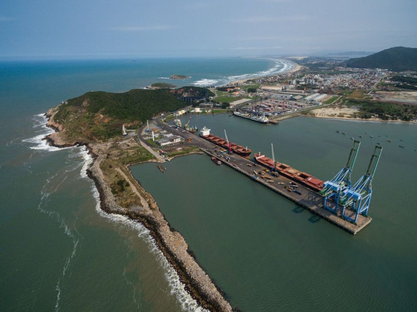 Vista aérea de um porto brasileiro, com docas, guindastes e navios junto à costa.