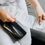 Mãos de uma mulher manuseiam vários recibos retirados de uma carteira preta.