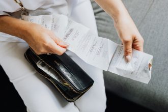Mãos de uma mulher manuseiam vários recibos retirados de uma carteira preta.